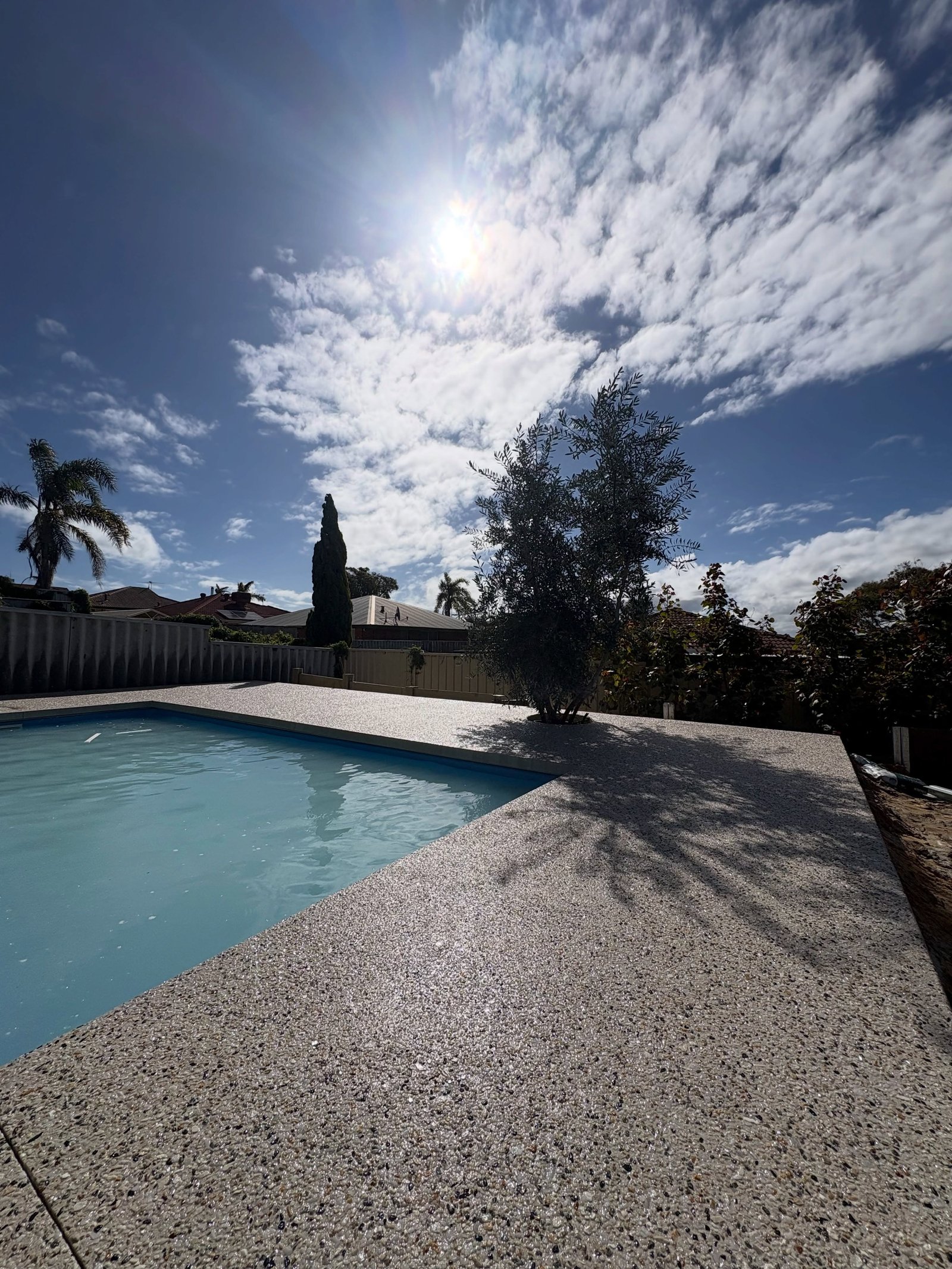 Exposed aggregate pool deck wrapping a backyard pool